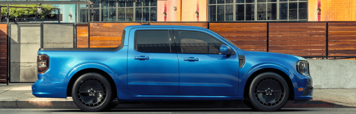 A blue Ford Maverick in profile parked by the curb.