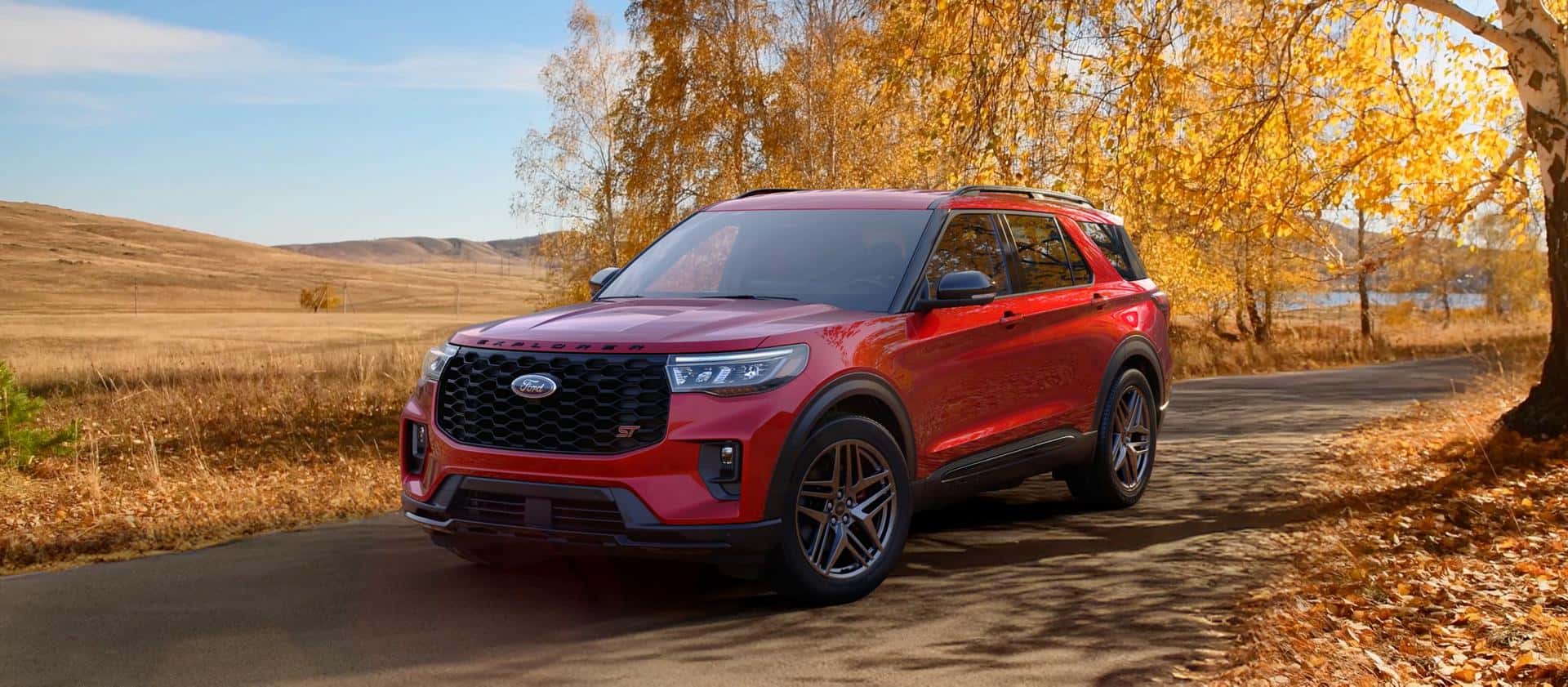 A red Ford Explorer driving by a field under autumn trees