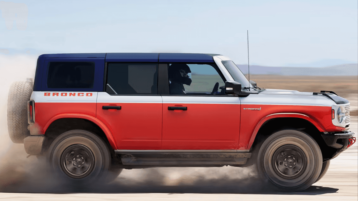 A red and white Ford Bronco kicking up dust as it drives on a desert path.