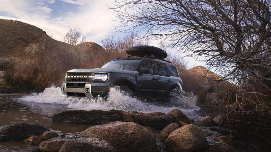A blue Ford Bronco Sport driving through a creek.