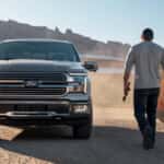 A dark gray Ford F-150 on a ranch next to a red tractor.