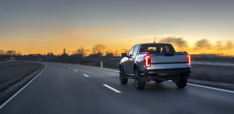 A silver pickup truck driving on the road as the sun sets.