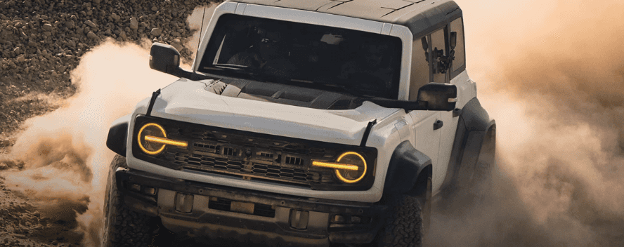 A white Ford Bronco kicking up dust as it drives off-road.