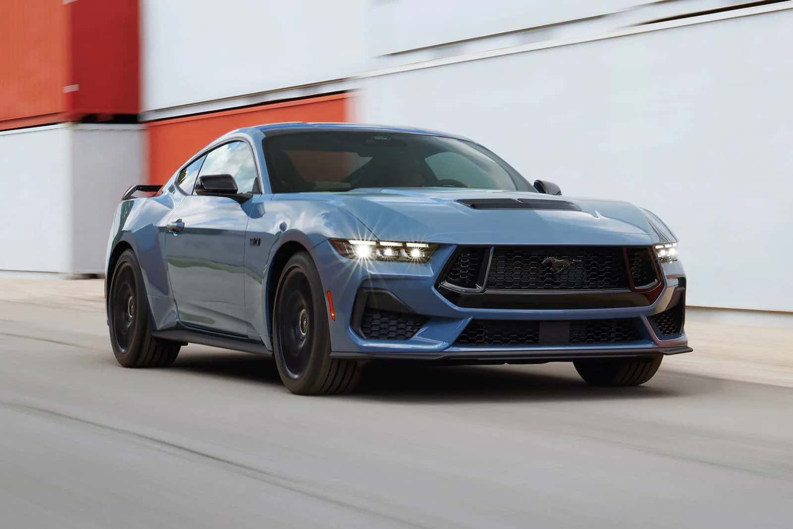 a blue 2026 ford mustang driving on a road near an industrial building