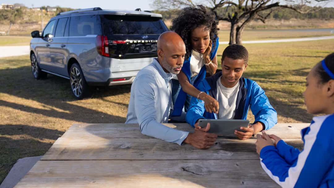 a family sitting at a table next to a 2026 Ford Expedition