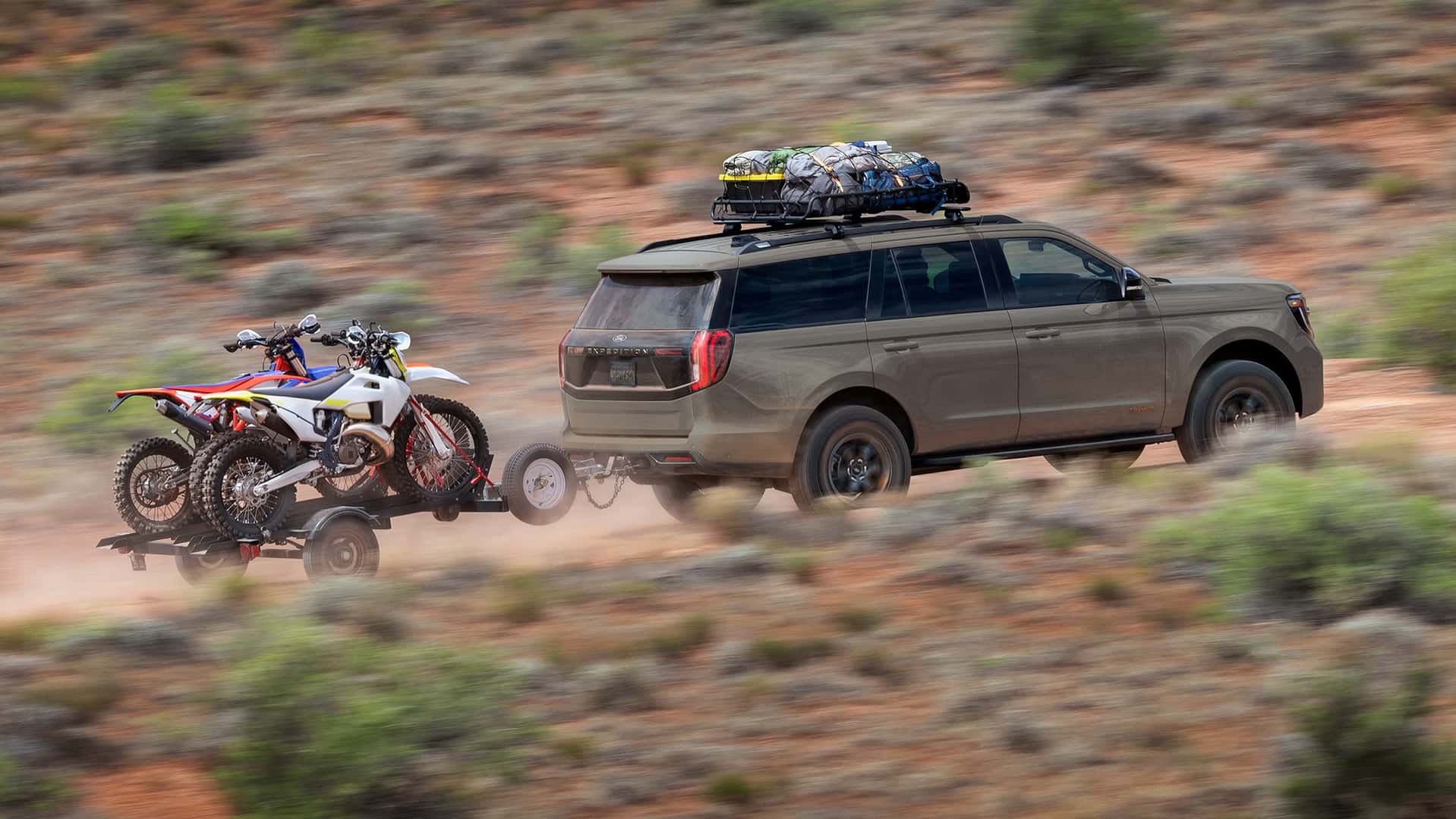 ford expedition towing dirt bikes on a desert dirt path.