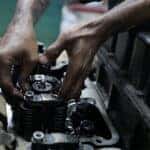 A person is working on a car engine with hands marked with oil
