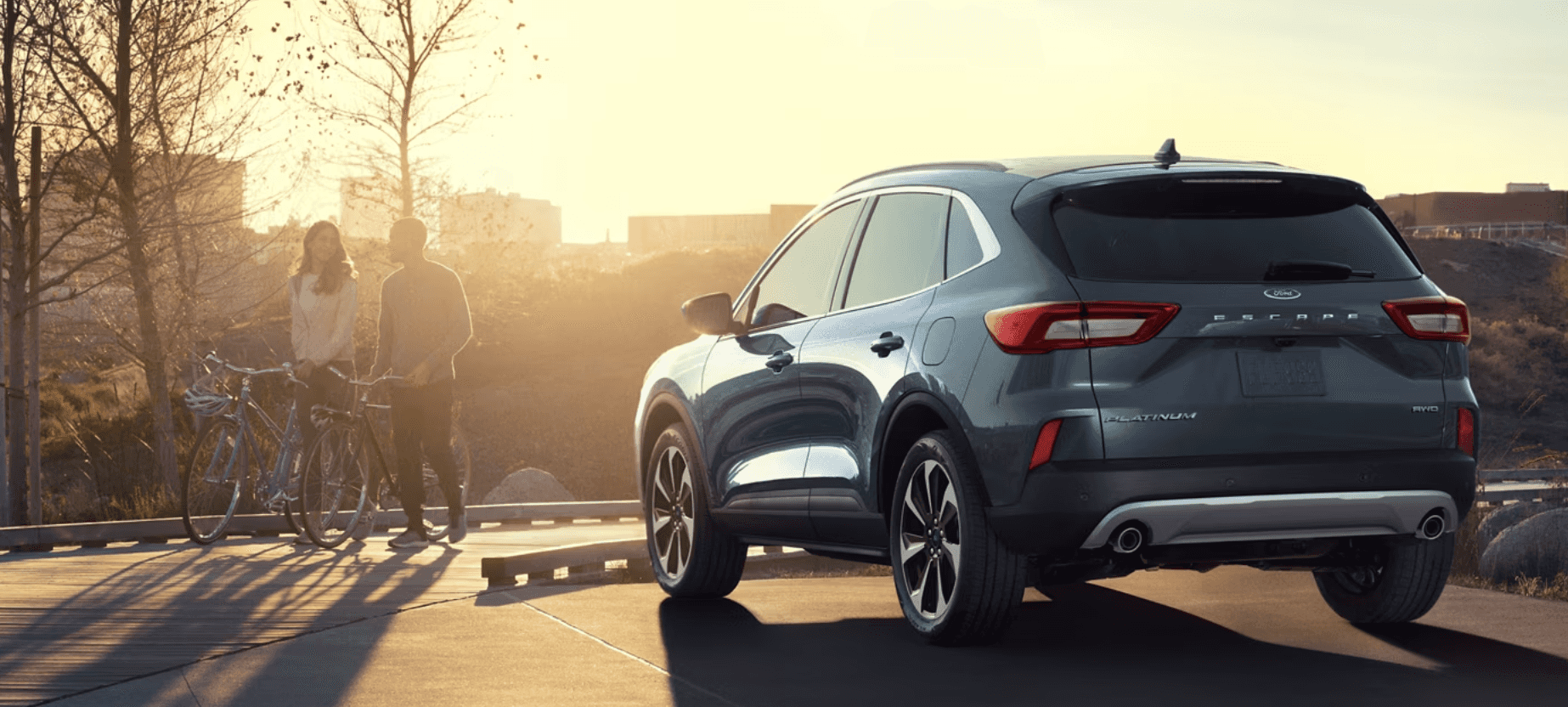 A couple walking near a new Ford Escape parked in the sunset
