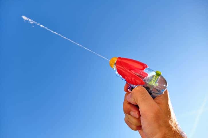 Colorful water pistol in man's hand against blue sky