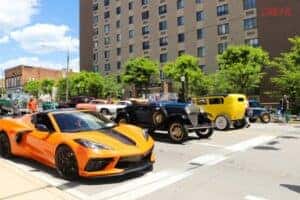 a modern orange car next to a black historical vehicle on the street