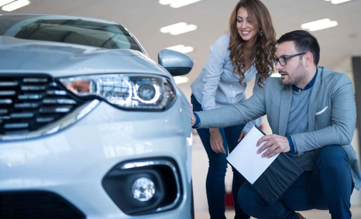 A man and woman in a car showroom inspect a silver vehicle.