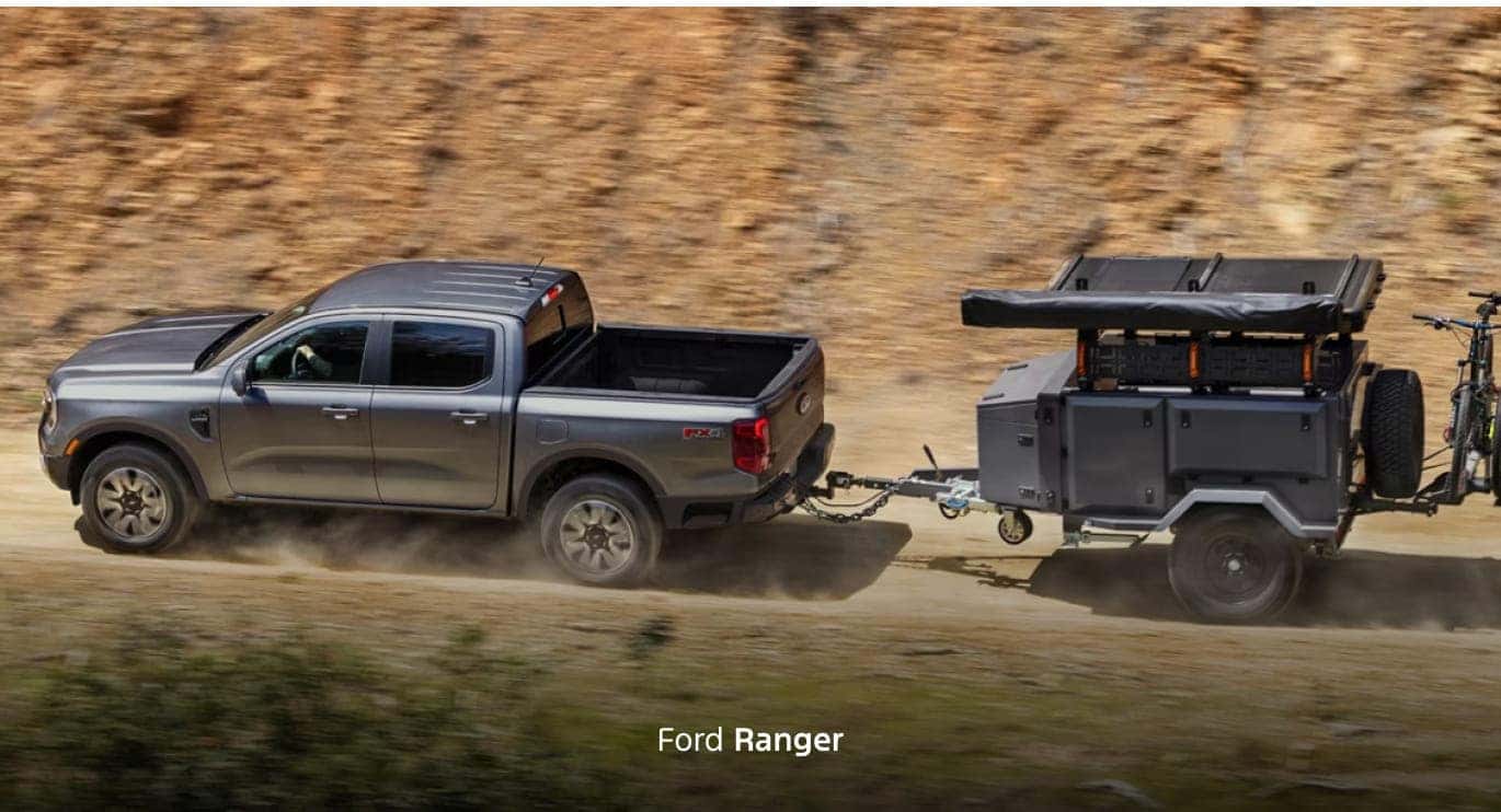 Gray Ford Ranger towing a compact utility trailer with outdoor gear and bicycles along a dusty off-road trail.