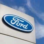 Close-up Ford brand logo on against blue sky background. Dealership centre of car shop