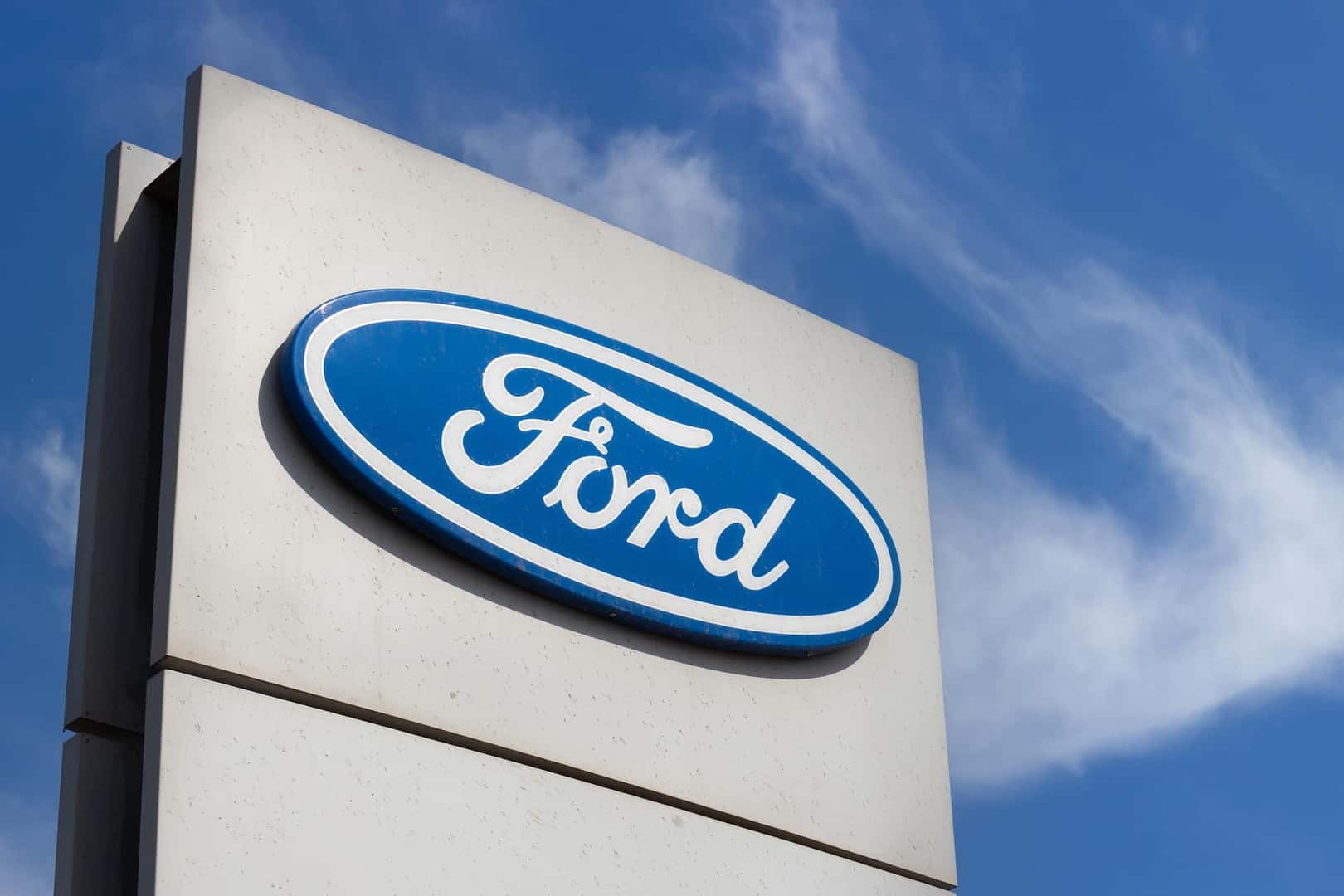 Close-up Ford brand logo on against blue sky background. Dealership centre of car shop