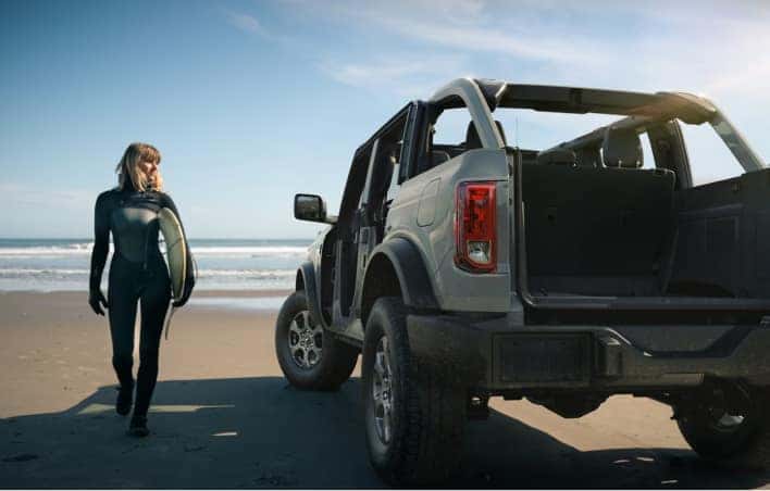 Surfer walking to her car parked on the beach