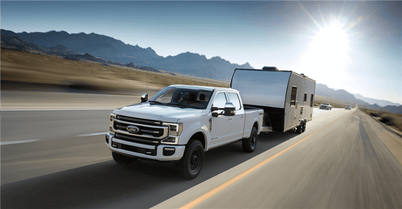 Ford F-150 driving with trailer hitched on open road near Upland CA - Ford and Chevrolet Comparison