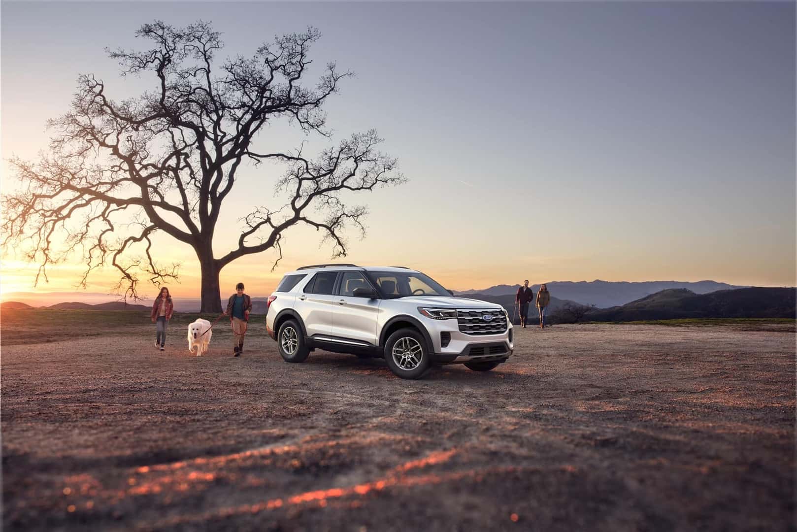 Ford Explorer parked by a large tree with a family playing with their dog nearby