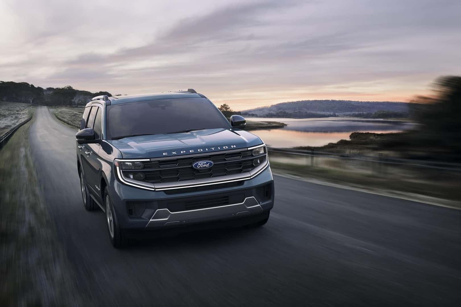 Front view of Ford Expedition driving down scenic road at sunset with motion blur