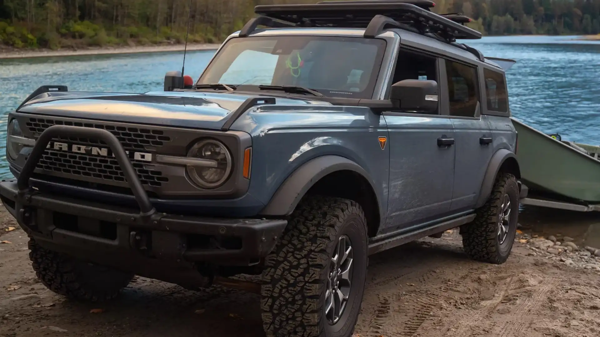 Exterior front-side view of a 2025 Ford Bronco® with off-road tires, roof rack, and tow setup near a river.