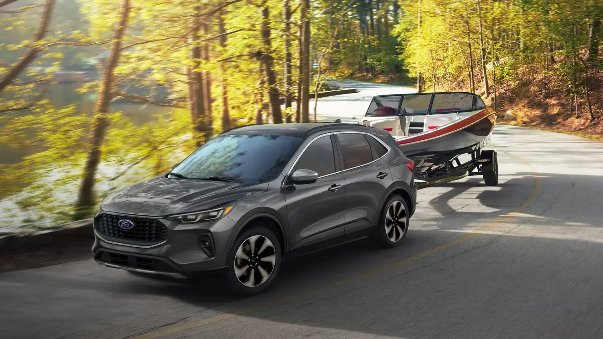 2025 Ford Escape® towing a boat along tree-lined lakeside road in daytime with motion blur effect.