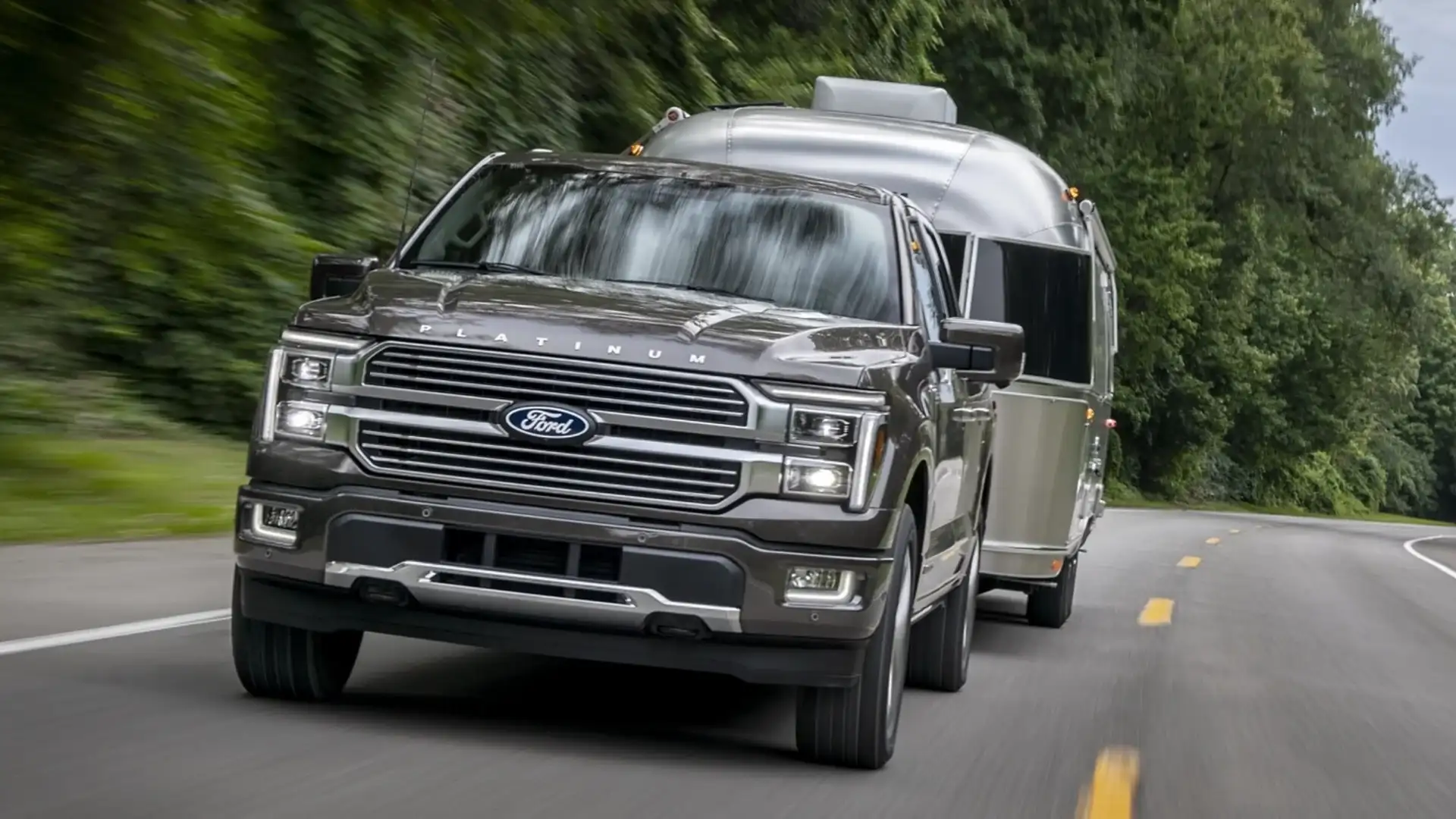 2025 Ford F-150® Platinum towing silver Airstream trailer on curved road, grille and LED lights visible.