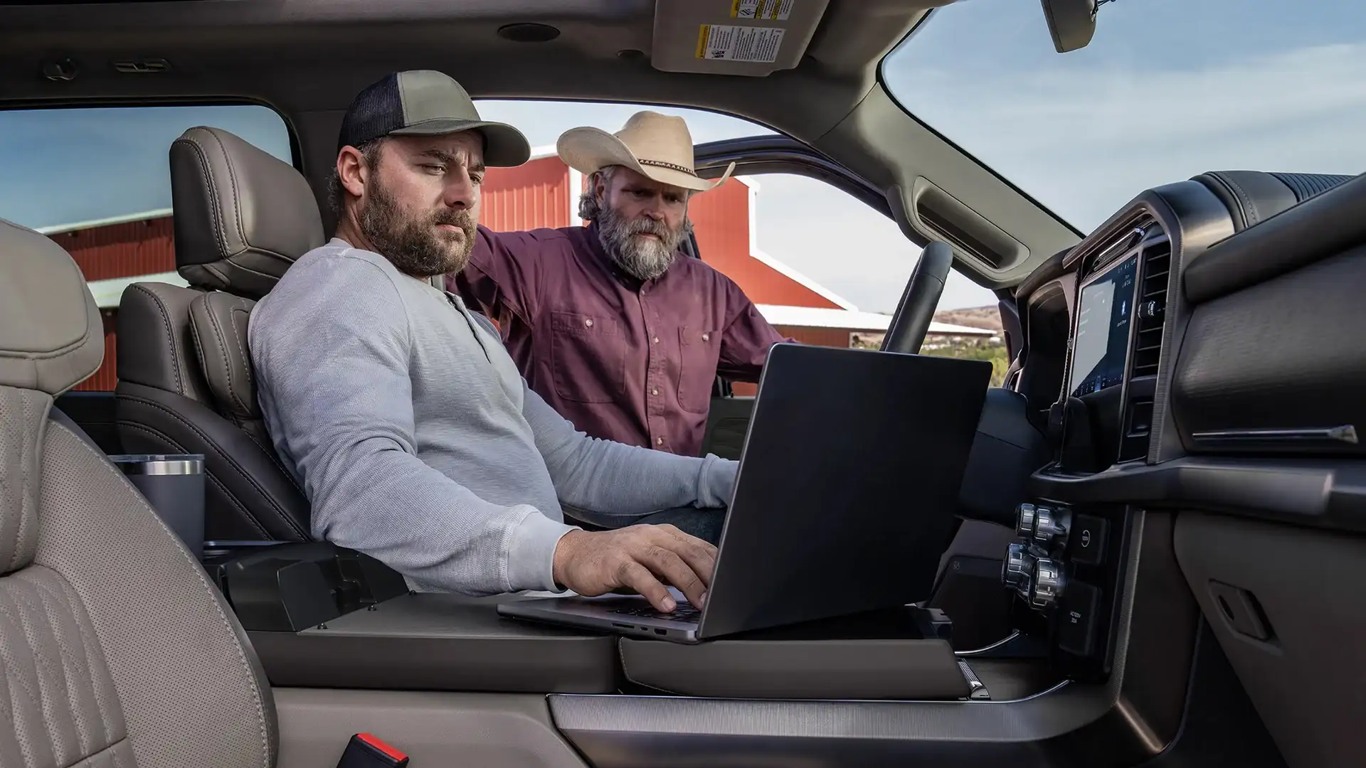 2025 Ford F-150® interior workspace with men using laptop on center console desk in farm setting.