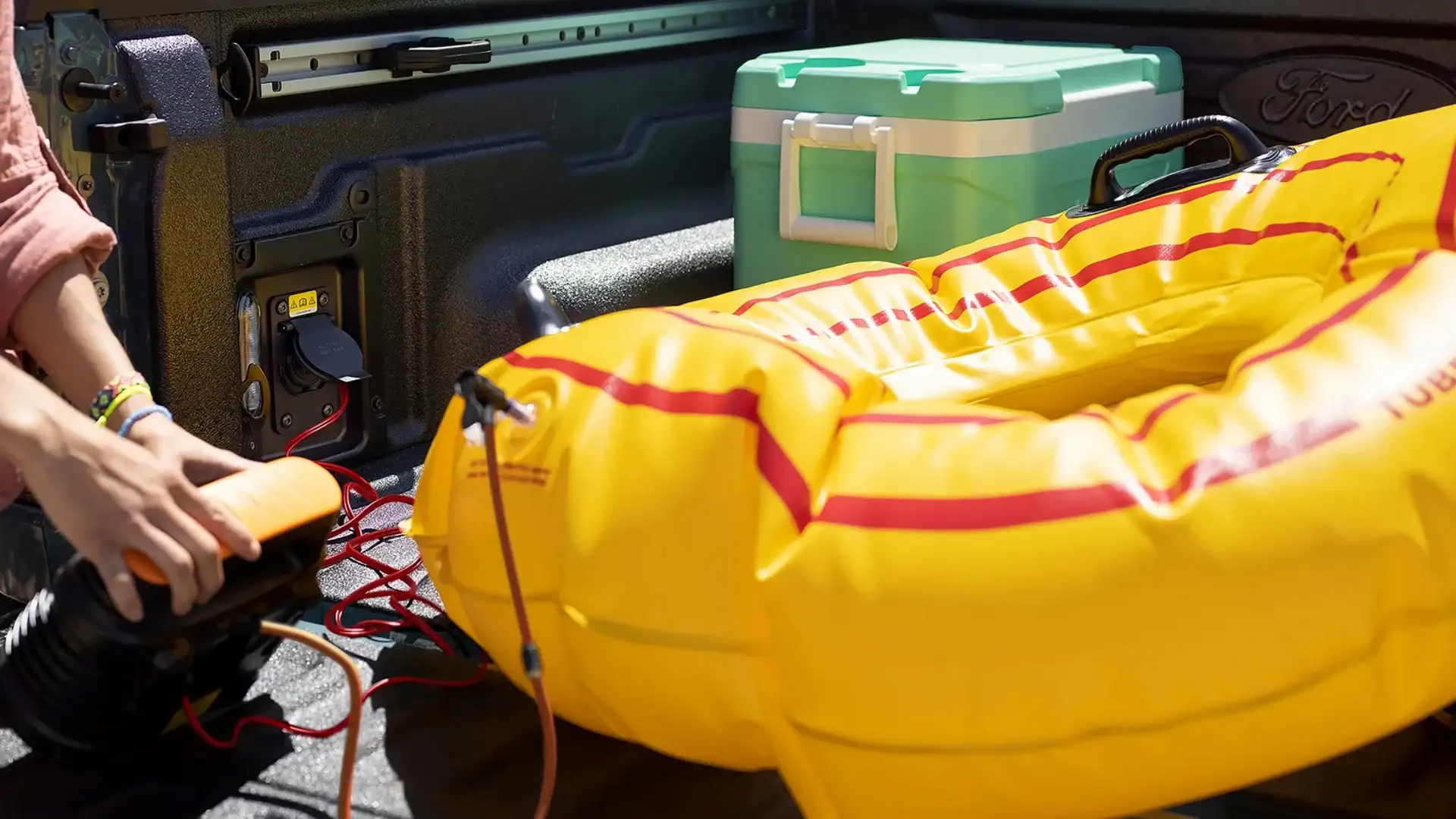 Truck bed of 2025 Ford Maverick® showing power outlet in use and loaded with cooler and inflatable tube.