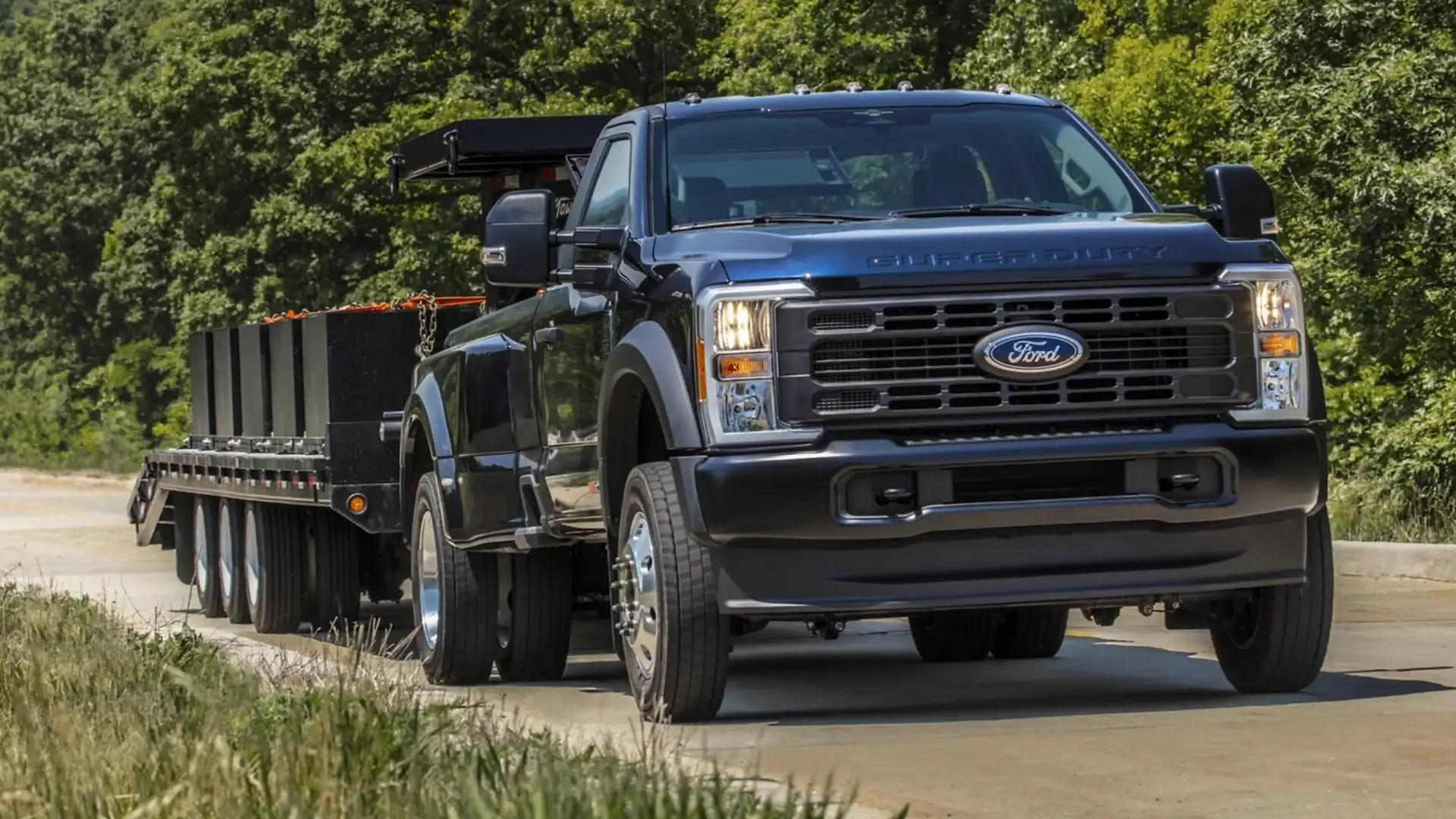 2026 Ford Super Duty® towing a multi-axle flatbed trailer loaded with cargo on rural pavement.