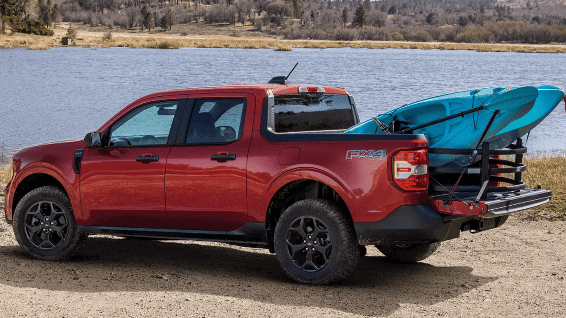Side profile of a red 2025 Ford Maverick® XLT FX4 with kayaks loaded in the truck bed by a lake.