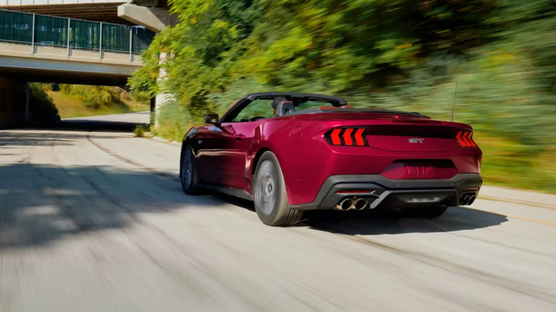 Rear view of a red 2025 Ford Mustang® convertible in motion, showcasing its athletic stance and triple-bar taillights.