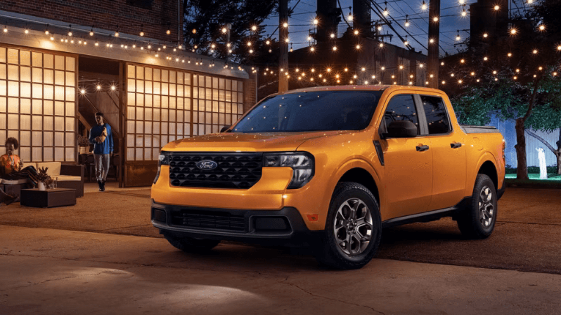 2026 Ford Maverick® compact pickup parked outdoors at night under string lights in urban setting.