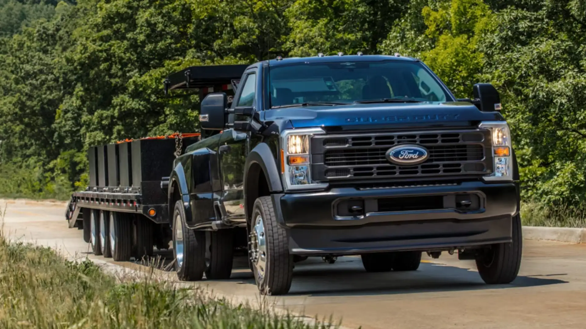 2026 Ford Super Duty® exterior front view towing flatbed trailer on highway.