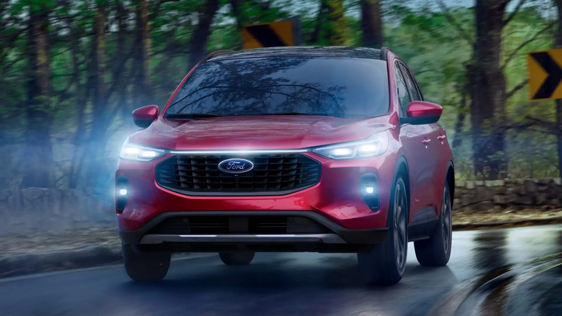 2026 Ford Escape® front view in red driving on winding forest road with LED headlights on.