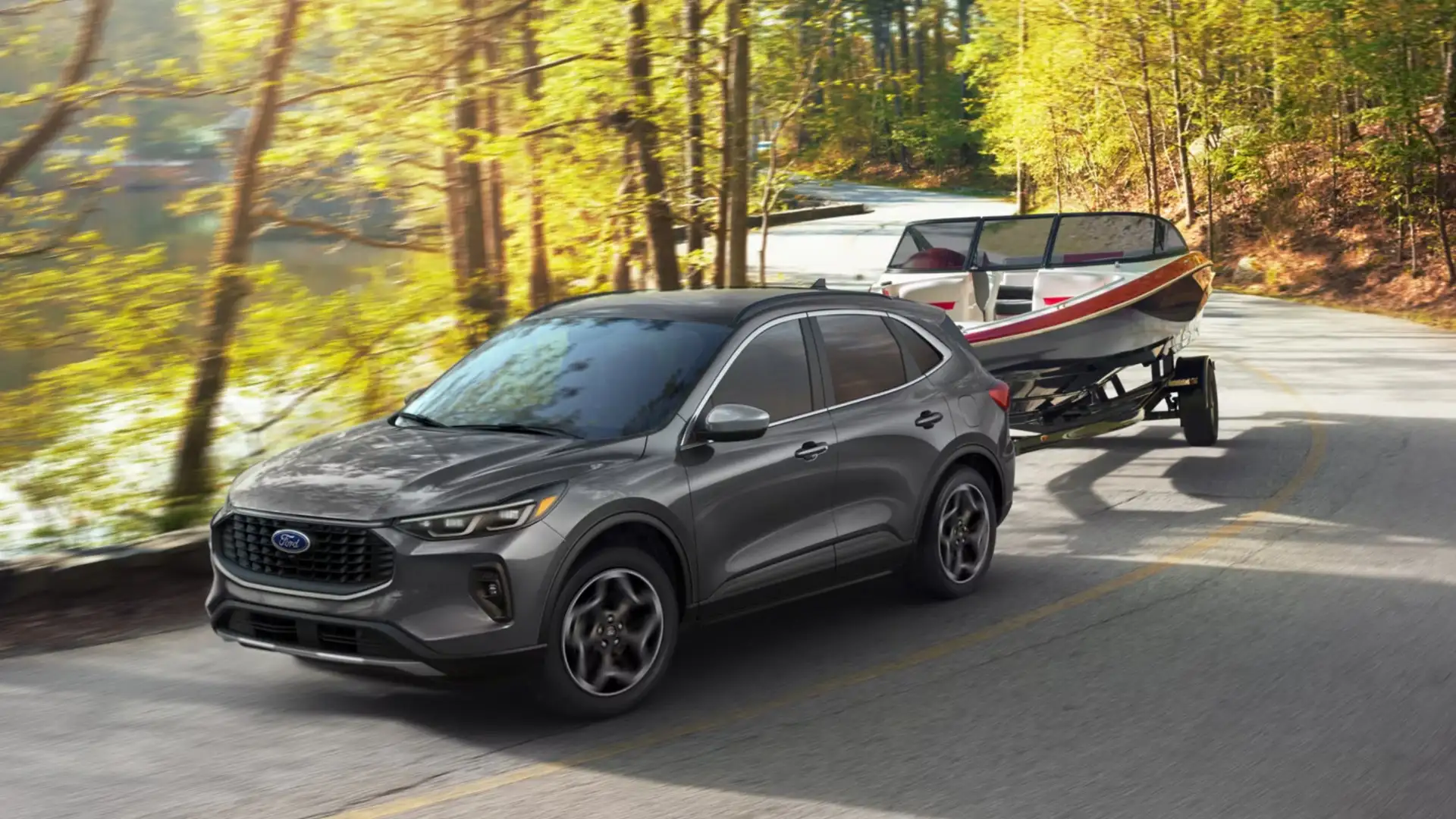 2026 Ford Escape® towing a boat along a scenic route, demonstrating its towing capabilities with a sleek silver exterior.