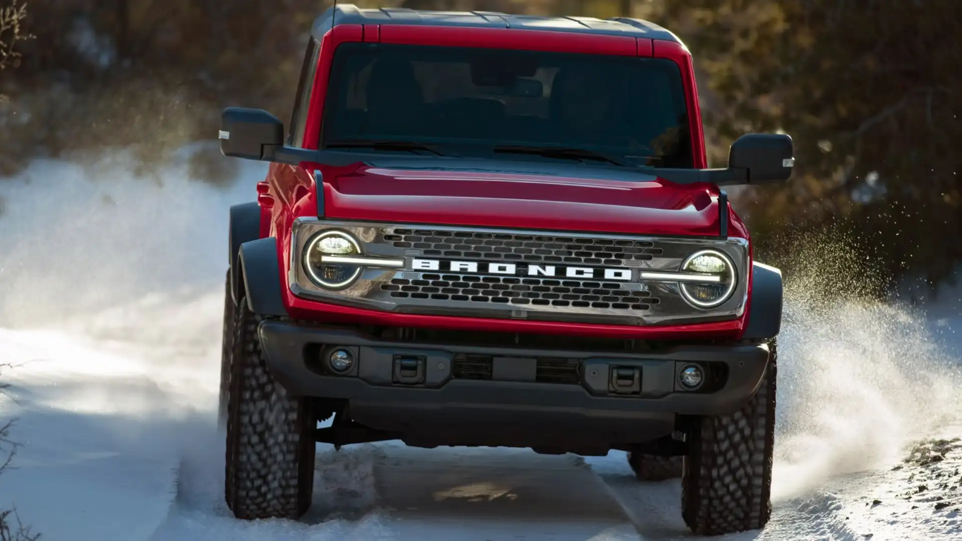 Front view of red 2025 Ford Bronco® driving through snow with off-road tires, round LED headlights, and signature BRONCO grille.