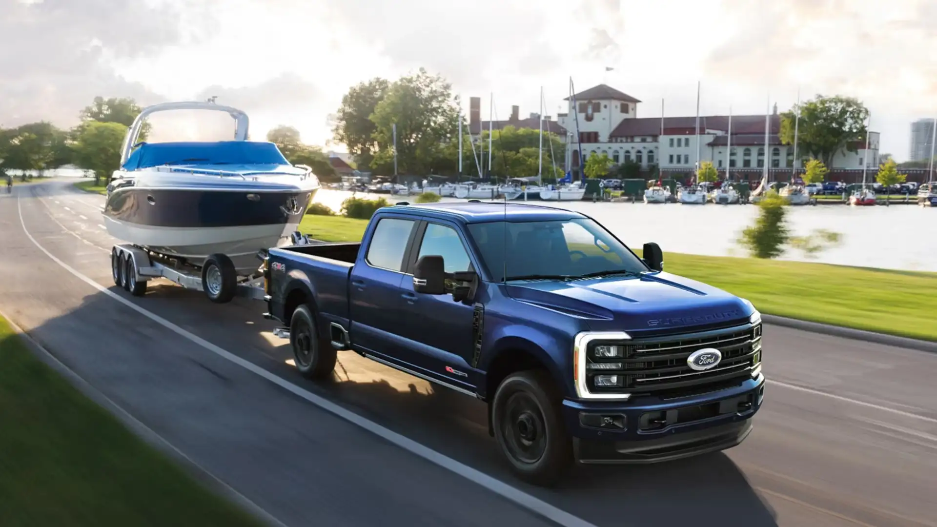 2026 Ford Super Duty® towing boat on trailer along waterfront road near marina.