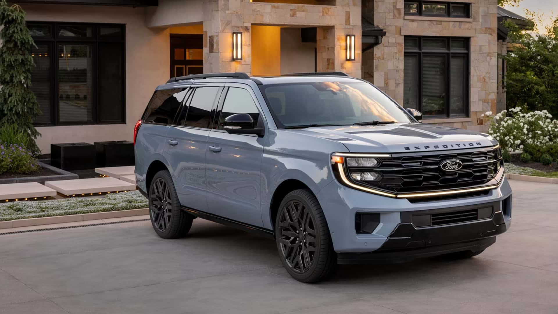 2026 Ford Expedition® full-size SUV parked in a modern home driveway, front three-quarter view with LED headlights and black wheels.