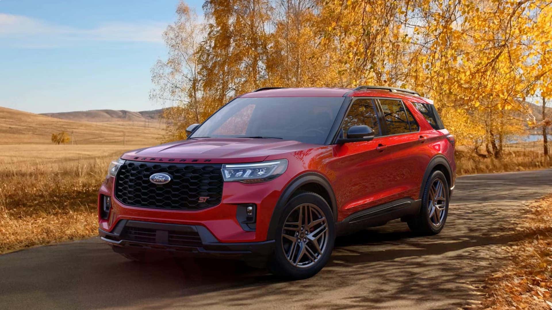 2026 Ford Explorer® in red parked on a road in autumn, front three-quarter view with golden trees and open fields in the background.