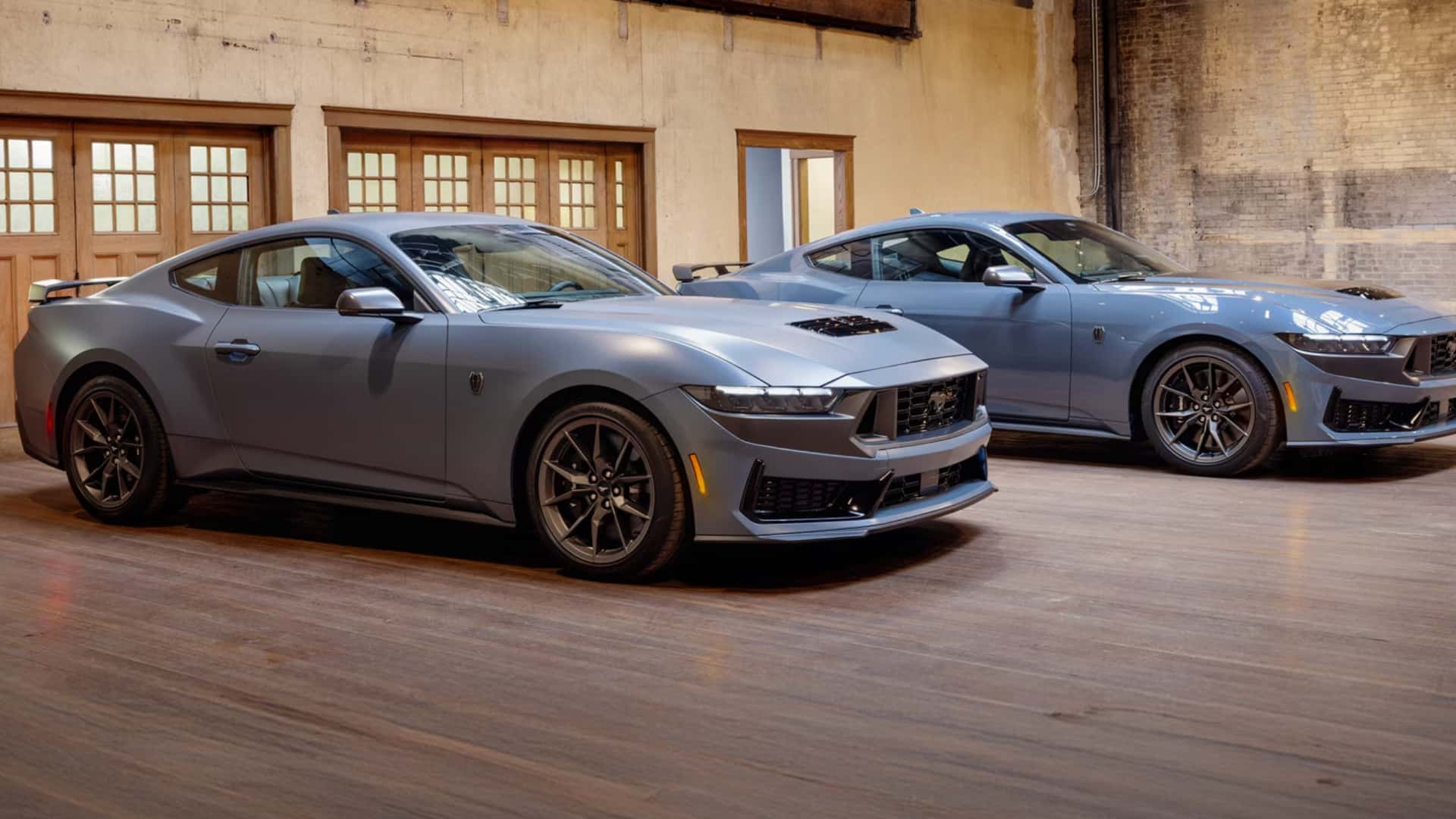 Two 2026 Ford Mustang® coupes parked indoors, front three-quarter view highlighting aggressive styling, hood vents, and performance wheels.