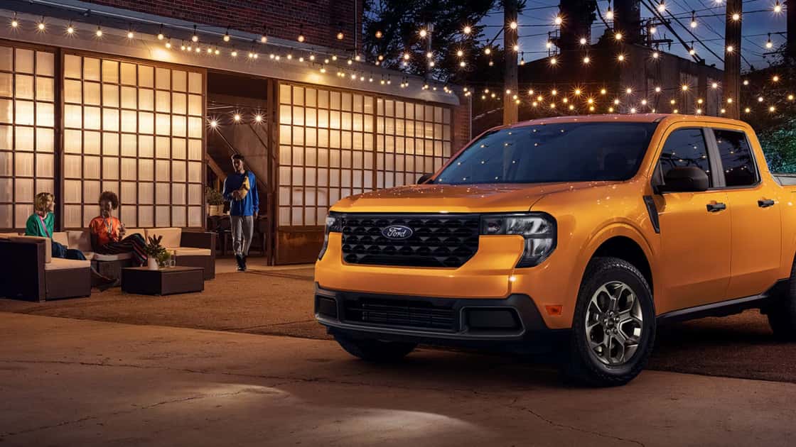 Yellow 2026 Ford Maverick® pickup truck with crew cab parked outside a modern urban patio, people in background..