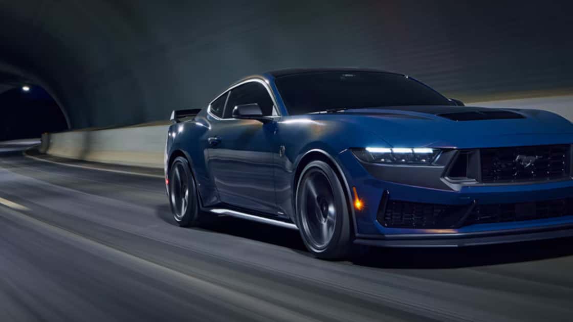 Blue 2026 Ford Mustang® sports car driving through a tunnel, emphasizing aggressive front design and headlamps..