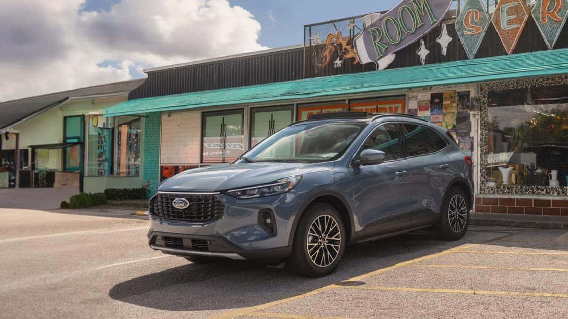 2026 Ford Escape® blue SUV parked outside a storefront with roof rails, alloy wheels, and compact crossover styling.