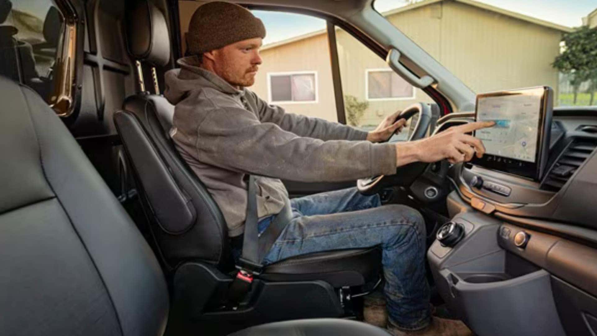2026 Ford E-Transit™ driver using the touchscreen inside the electric work van with black front seating.