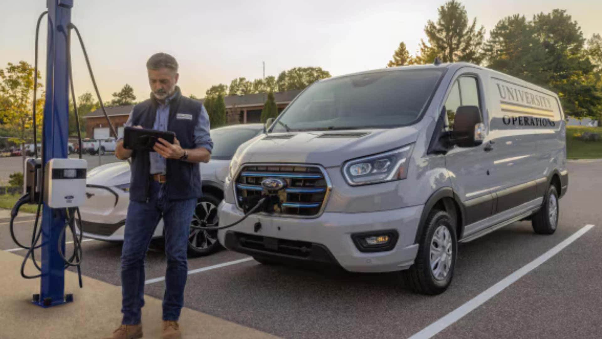 2026 Ford E-Transit™ electric van charging at a station with fleet manager using a tablet beside the vehicle.