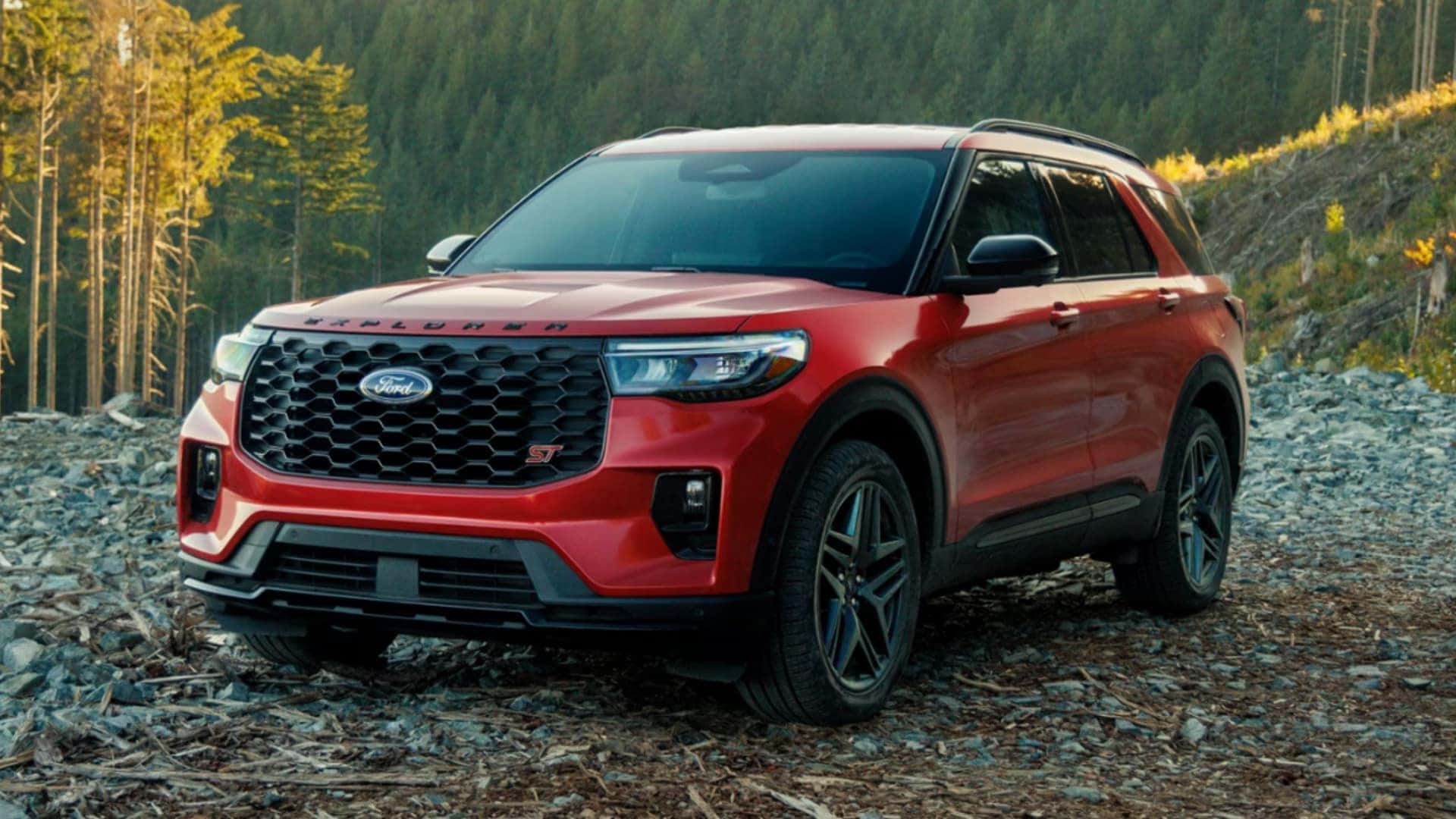2026 Ford Explorer® ST red SUV parked on a rocky forest trail with black grille, roof rails, and rugged styling.