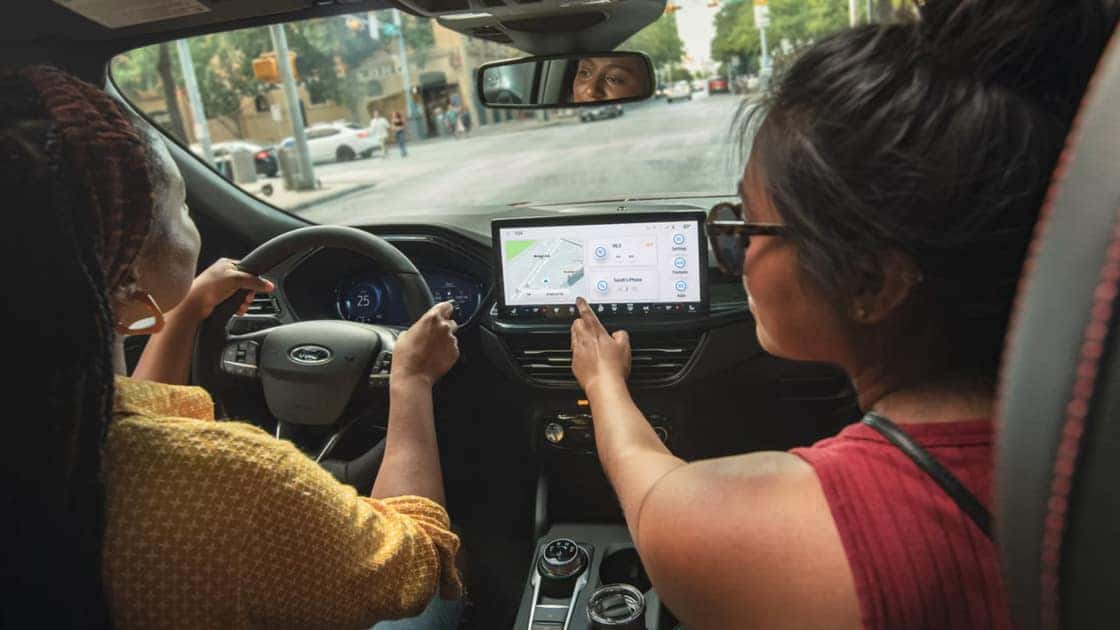 2026 Ford Escape® cabin with driver and passenger using touchscreen navigation in city traffic.