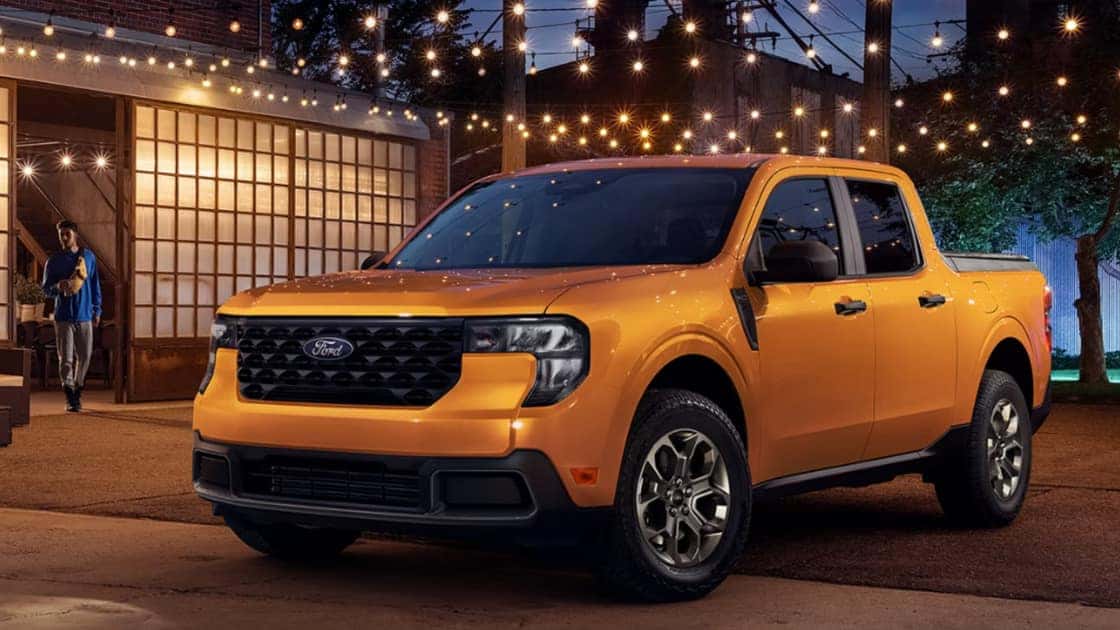 2026 Ford Maverick® yellow pickup parked at night near a home with string lights and bold styling.