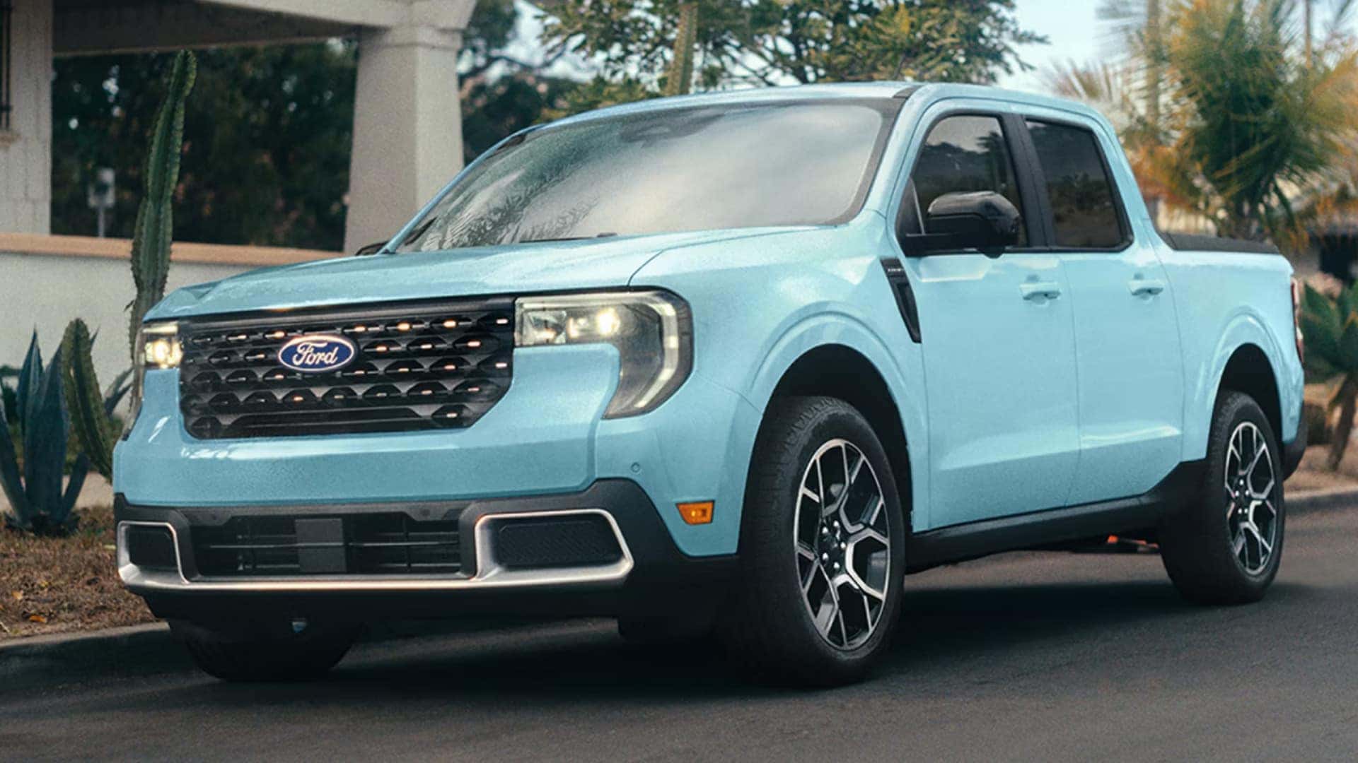 2026 Ford Maverick® in light blue driving on a neighborhood street with headlights on and pickup body styling.