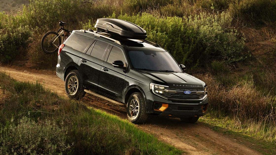 2026 Ford Expedition® SUV driving on a dirt trail with roof cargo, bike rack, and outdoor adventure gear.