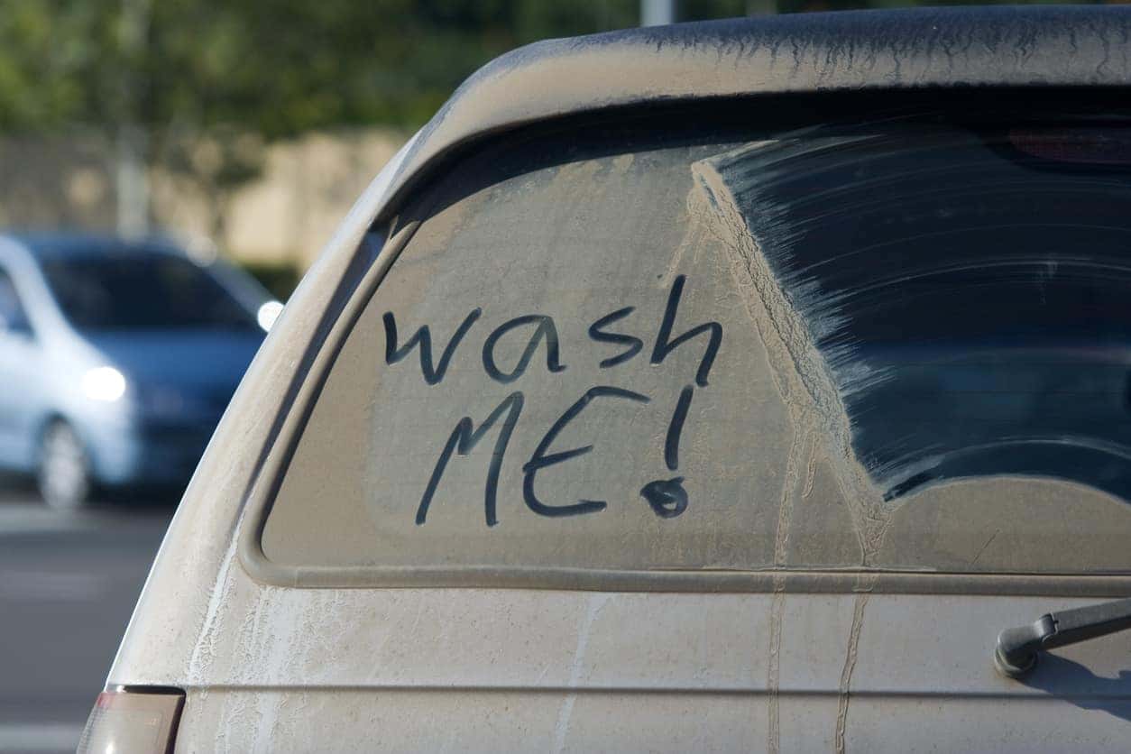A dirty car with wash me written in the dirt.